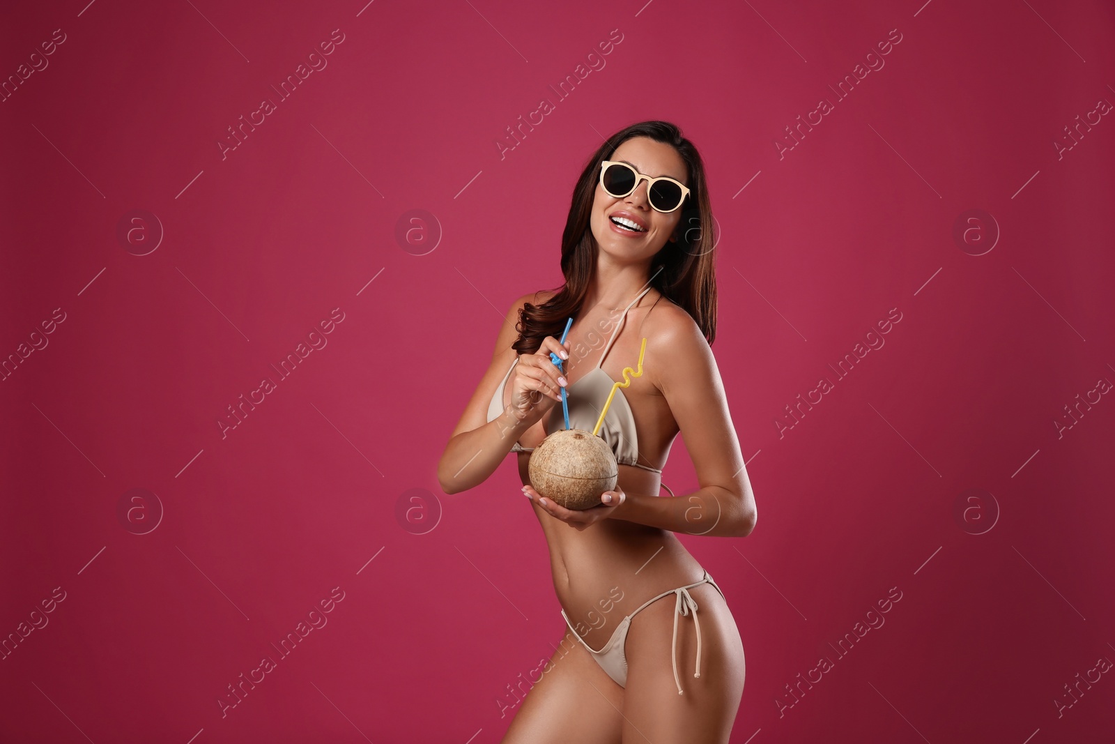 Photo of Beautiful woman in stylish bikini with tropical cocktail on crimson background