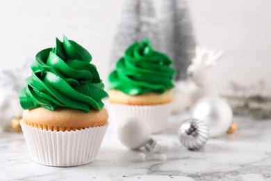 Delicious cupcakes with green cream and Christmas decor on white marble table