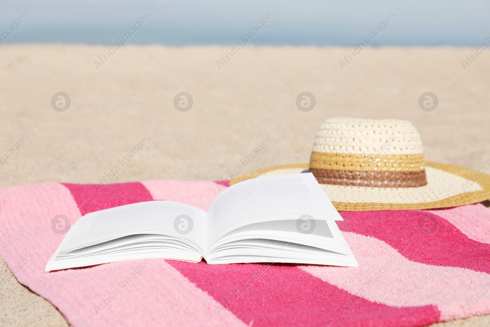 Photo of Open book, hat and striped towel on sandy beach near sea. Space for text