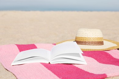Photo of Open book, hat and striped towel on sandy beach near sea. Space for text