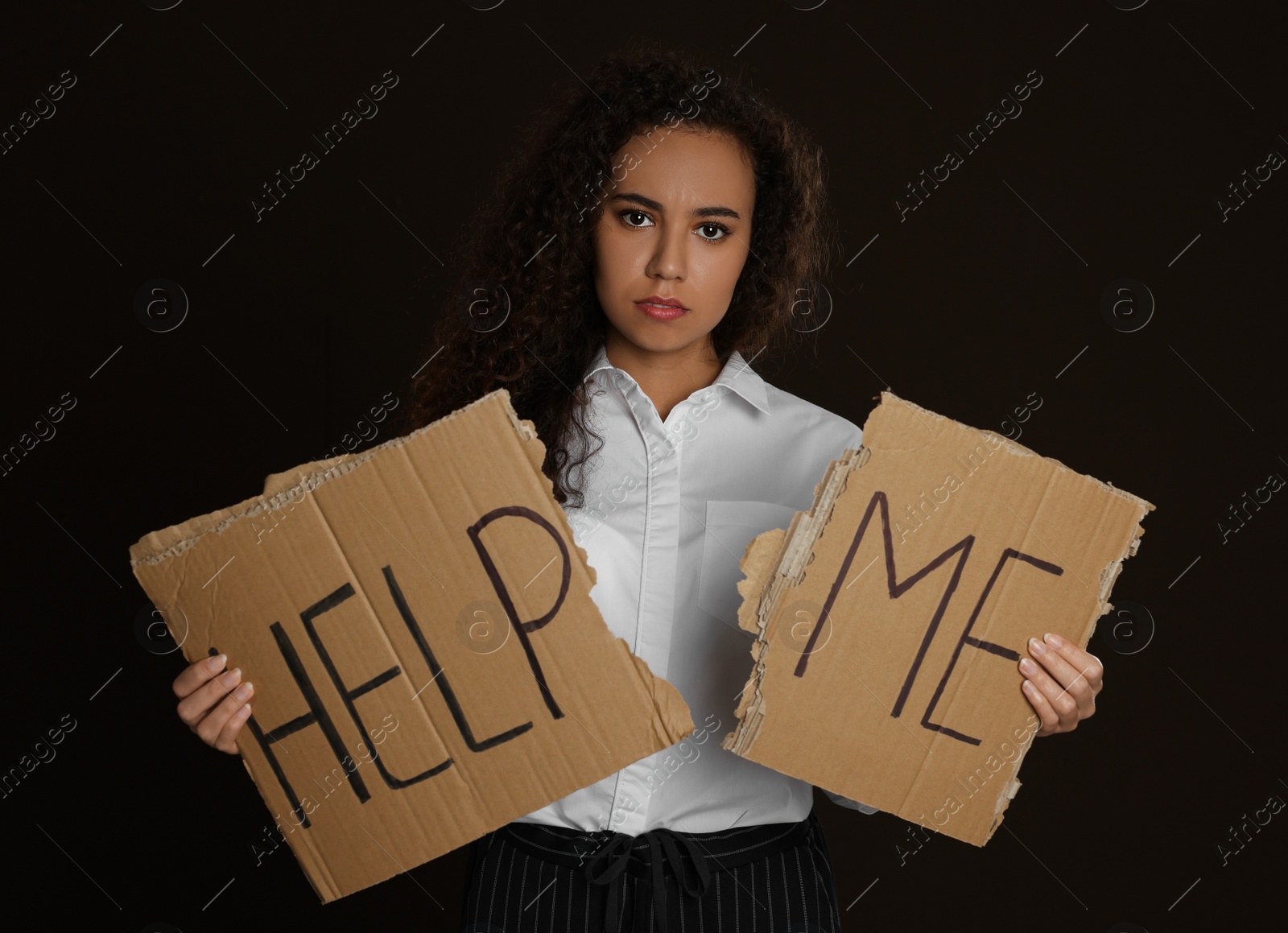 Photo of Unhappy African American woman with HELP ME sign on dark background