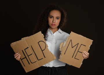 Photo of Unhappy African American woman with HELP ME sign on dark background