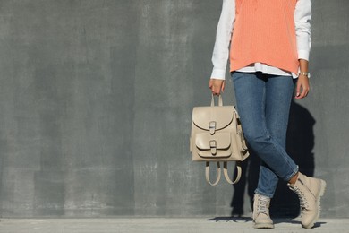 Photo of Young woman with stylish beige backpack near grey wall outdoors, closeup. Space for text