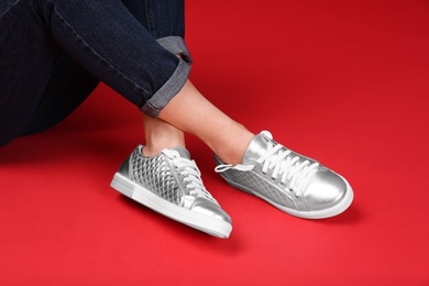 Woman in stylish sport shoes sitting on color background