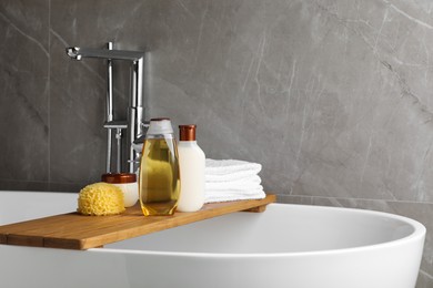 Wooden bath tray with shampoo, other toiletries and towels on tub indoors, space for text