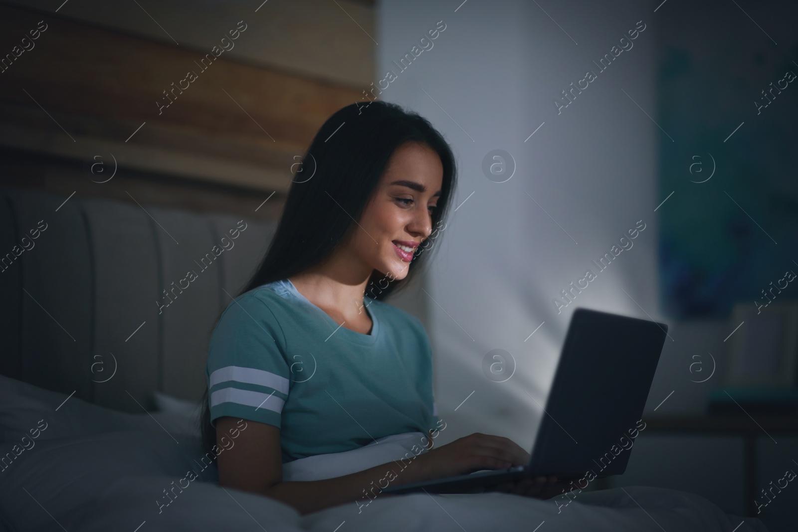 Photo of Young woman with nomophobia using laptop in bed at night. Insomnia concept