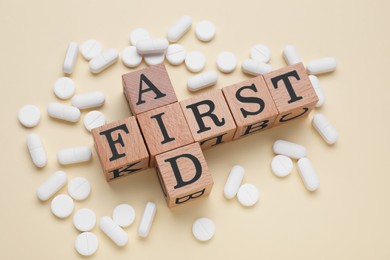 Words First Aid made of wooden cubes and pills on beige background