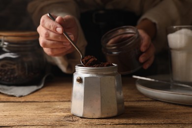 Photo of Woman putting ground coffee in moka pot at wooden table, closeup