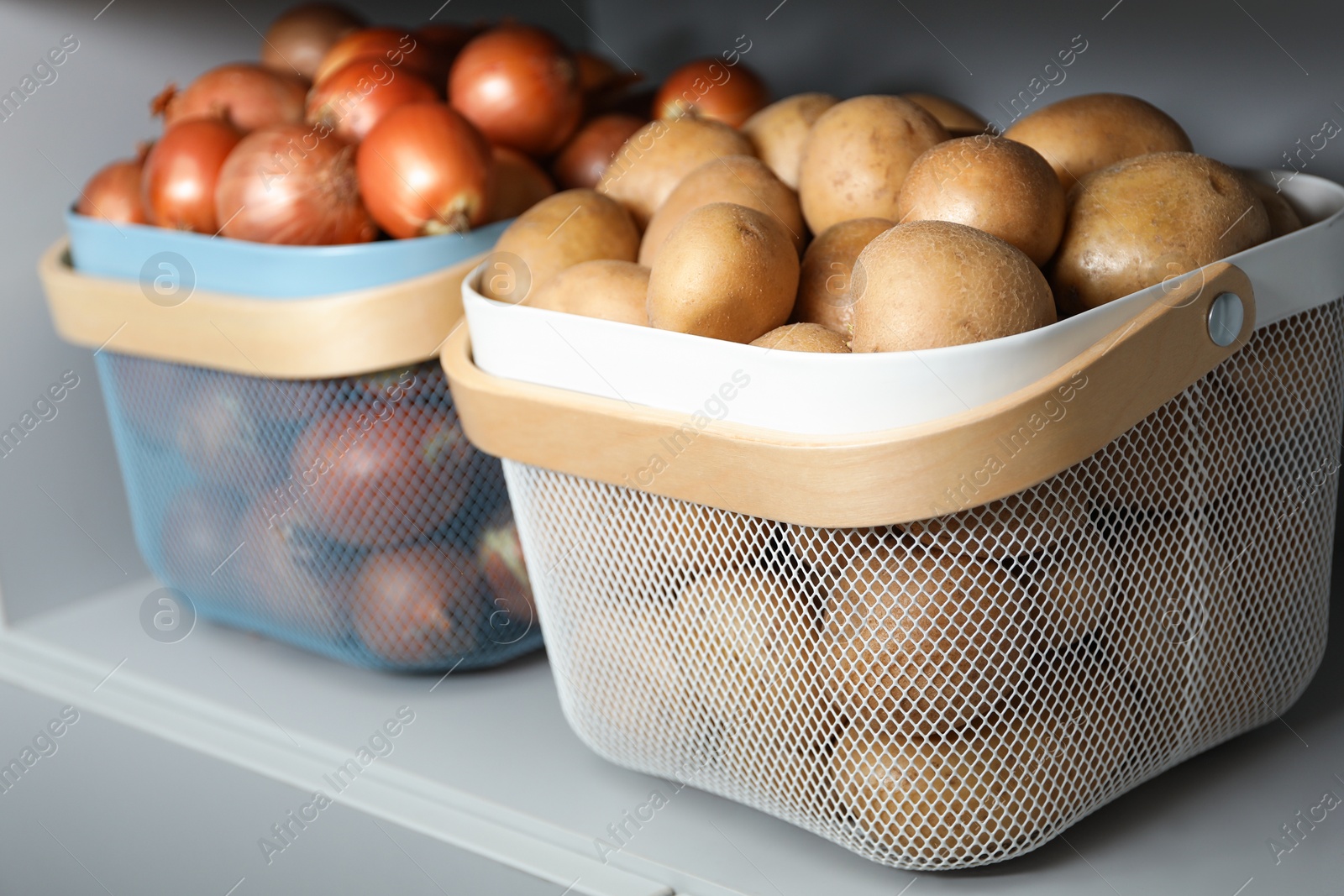 Photo of Baskets with potatoes and onions on shelf. Orderly storage