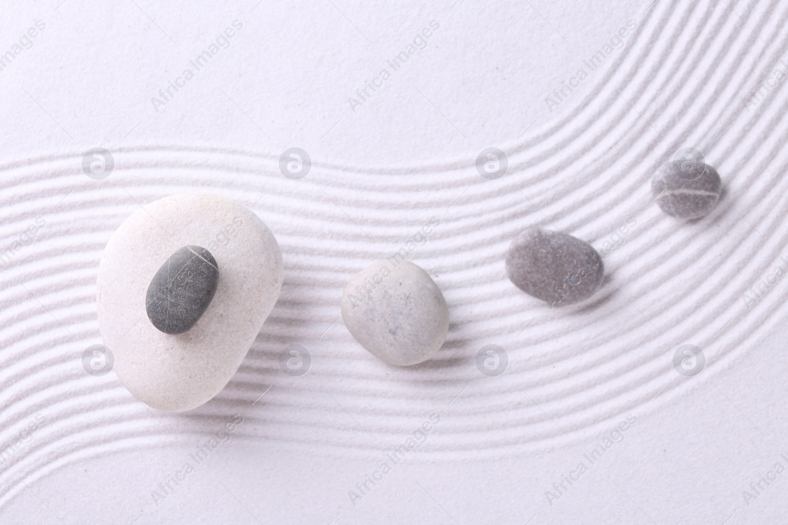 Photo of Zen garden stones on white sand with pattern, flat lay