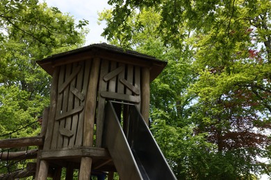 Wooden slide with bridge near big trees in park. Outdoor playground