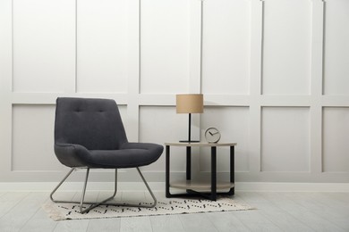 Modern grey armchair and small table near white wall indoors. Space for text