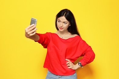 Attractive young woman taking selfie on color background