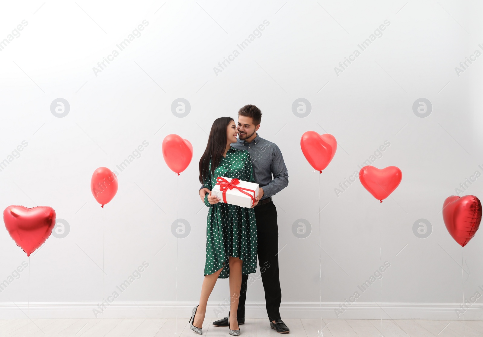 Photo of Happy young couple in room decorated with heart shaped balloons. Valentine's day celebration