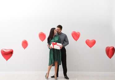 Photo of Happy young couple in room decorated with heart shaped balloons. Valentine's day celebration