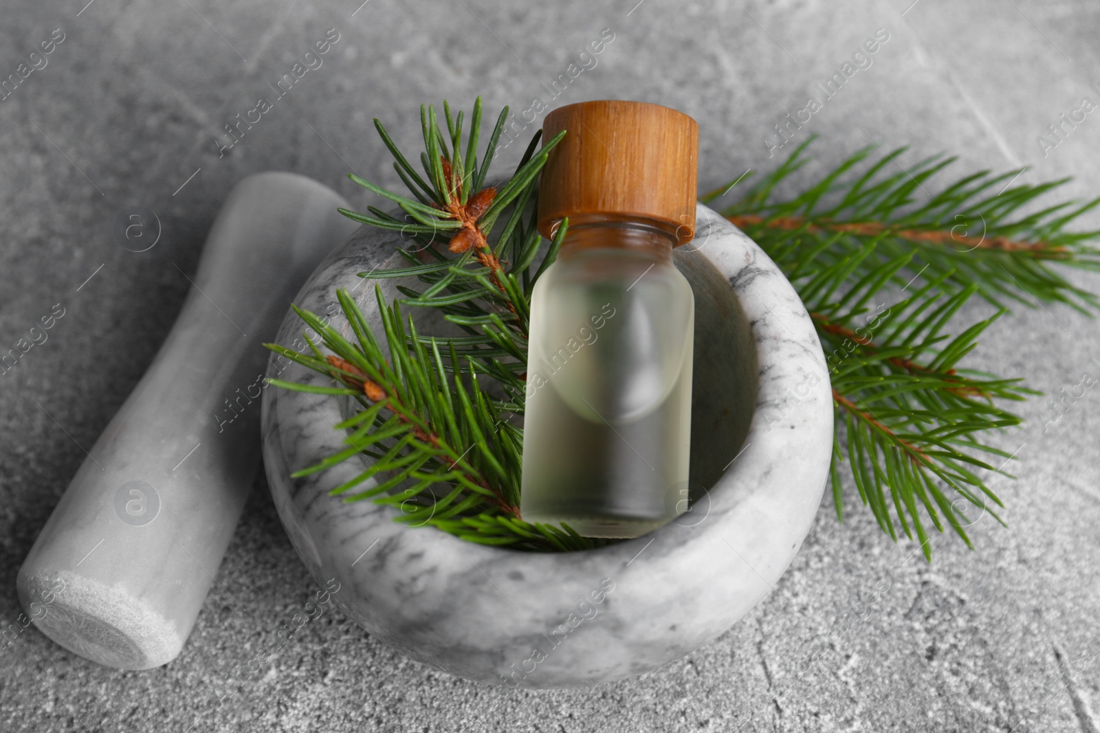 Photo of Bottle of aromatic essential oil and mortar with pine branch on light grey table, closeup