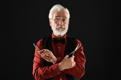 Senior man with mustache holding blade and scissors on black background