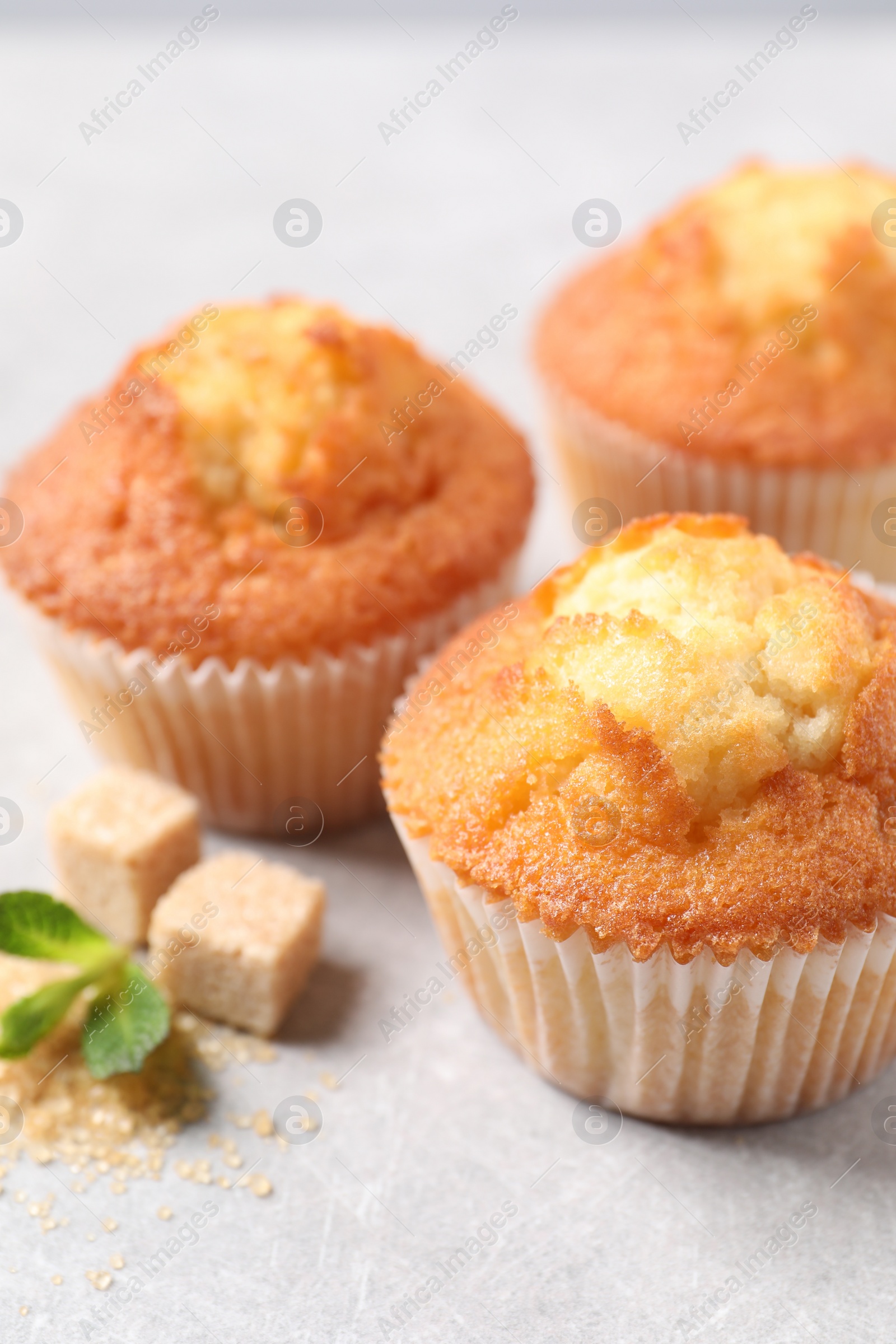 Photo of Delicious sweet muffins and brown sugar on light grey textured table, closeup. Space for text