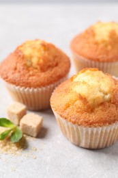 Photo of Delicious sweet muffins and brown sugar on light grey textured table, closeup. Space for text
