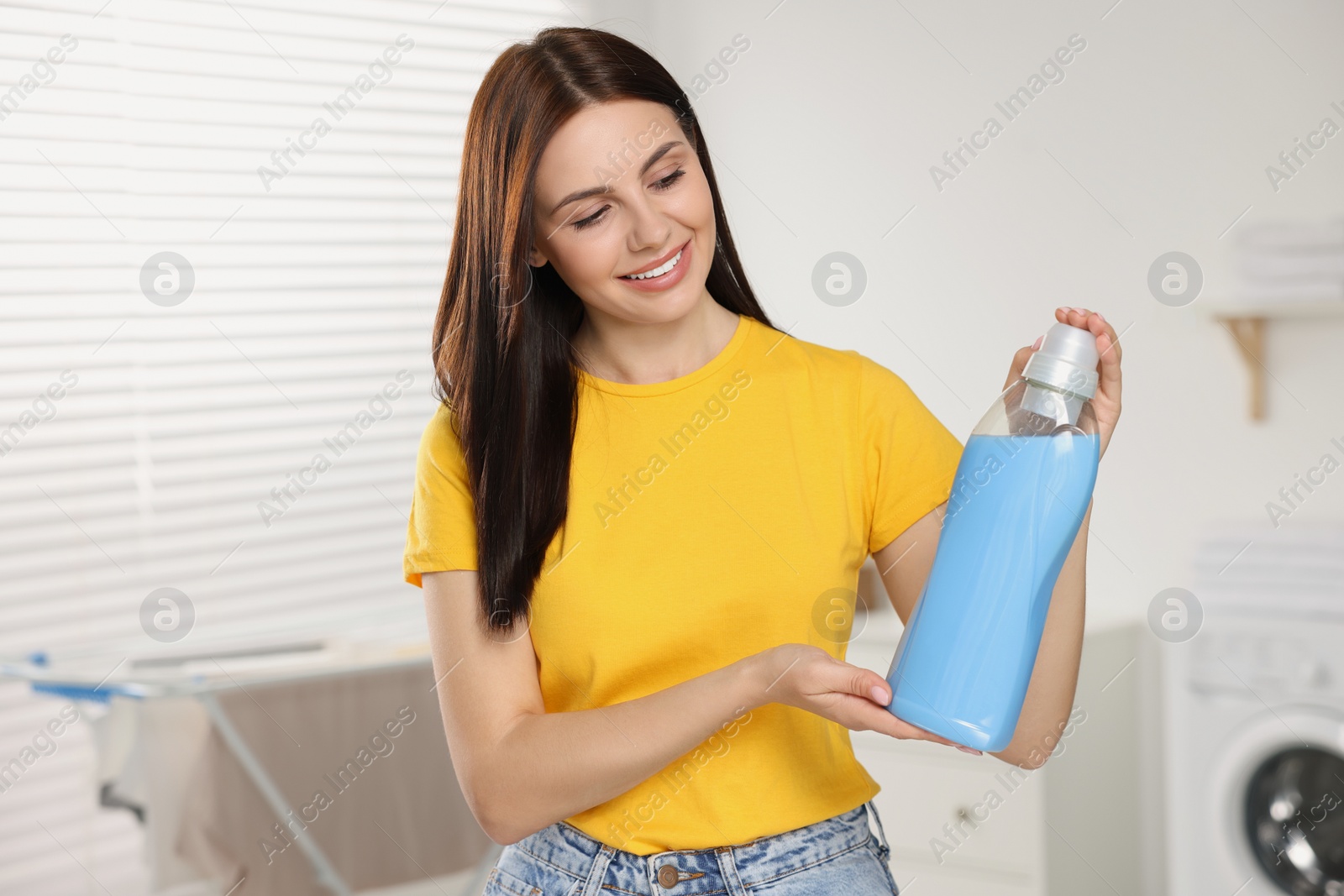 Photo of Beautiful woman holding fabric softener in bathroom