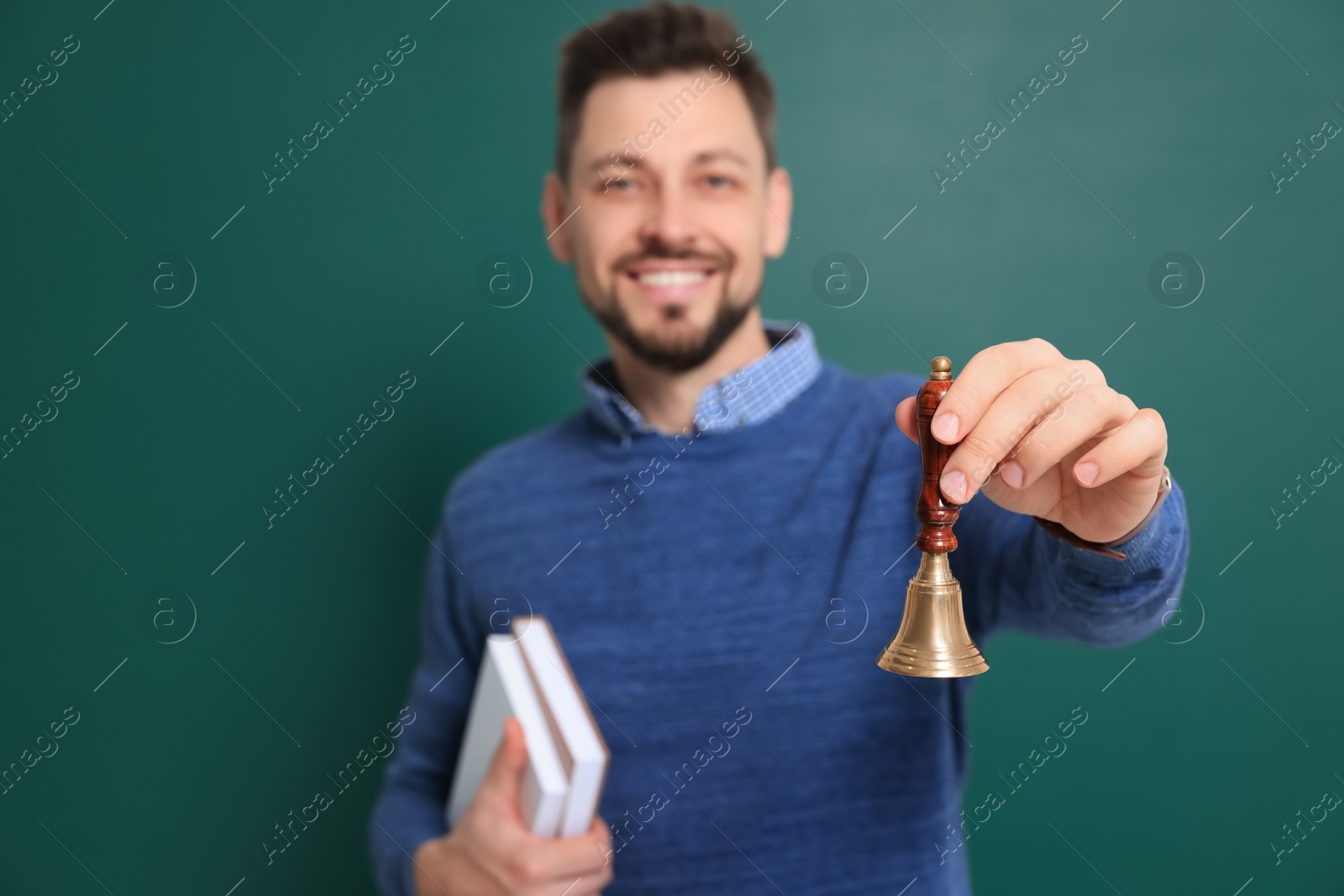 Photo of Teacher with school bell near chalkboard. Focus on hand