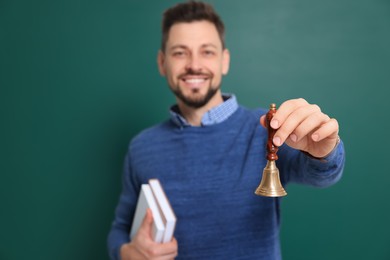Photo of Teacher with school bell near chalkboard. Focus on hand
