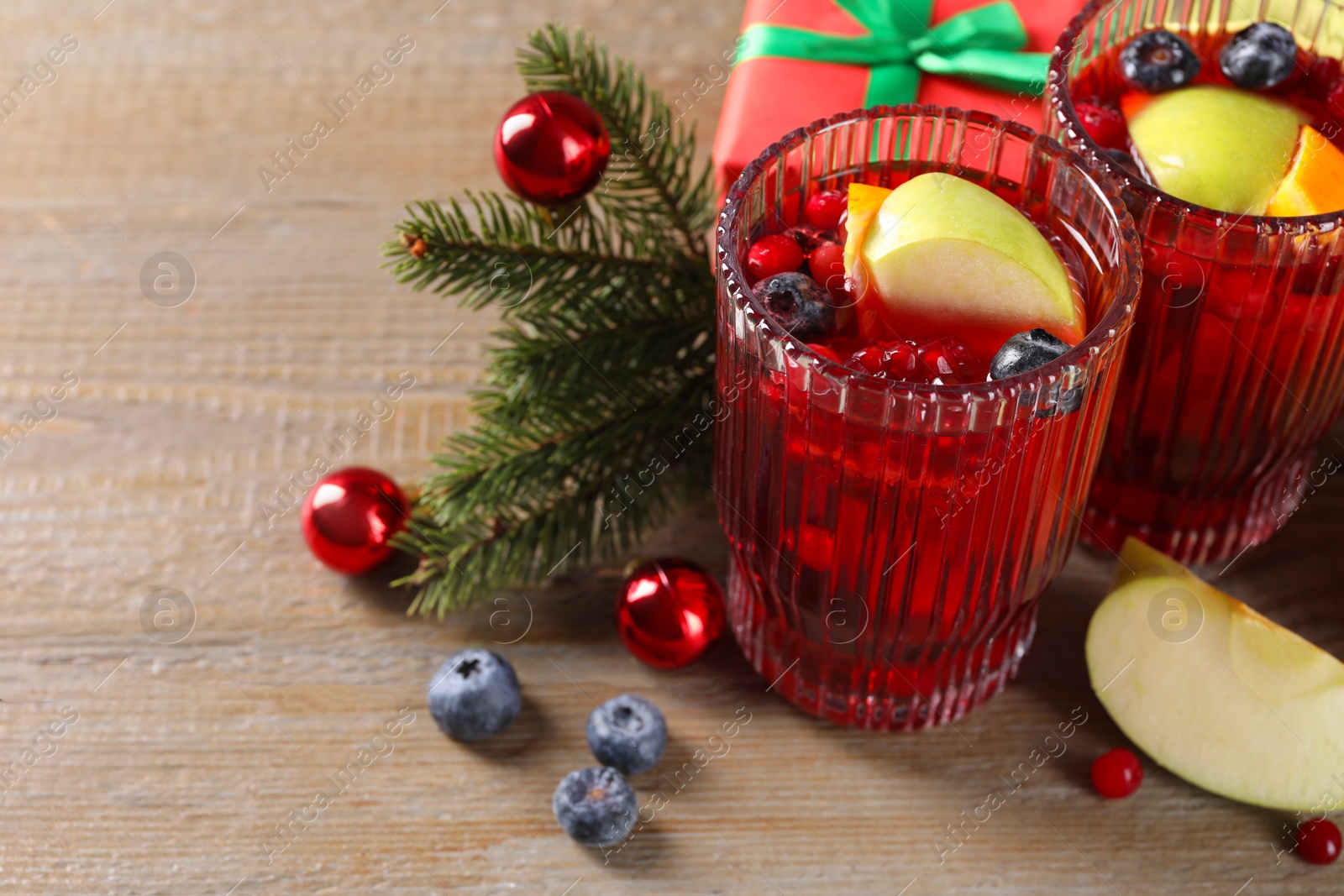 Photo of Aromatic Sangria drink in glasses, ingredients and Christmas decor on wooden table. Space for text