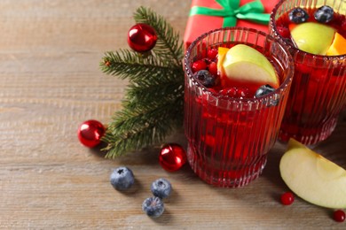 Photo of Aromatic Sangria drink in glasses, ingredients and Christmas decor on wooden table. Space for text