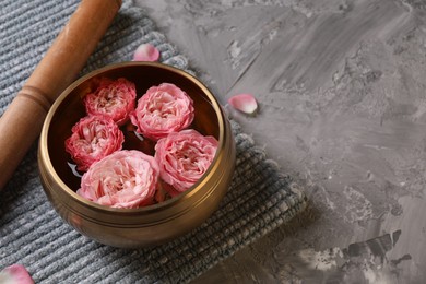Tibetan singing bowl with water, beautiful roses and mallet on grey textured table, space for text