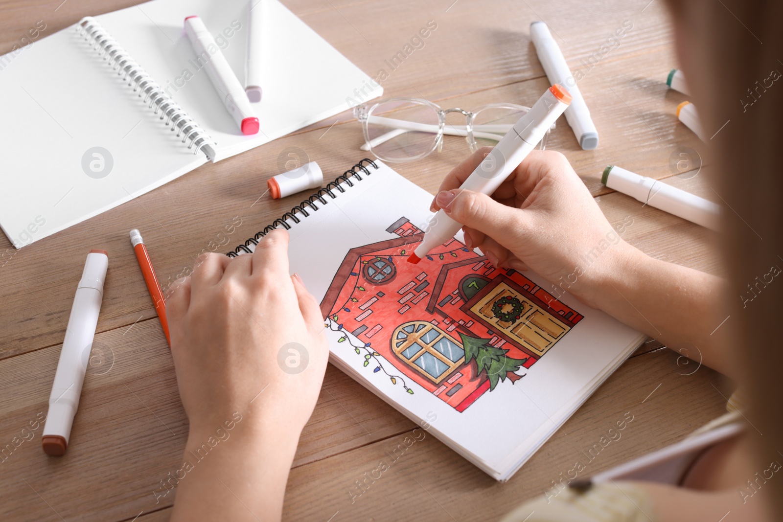 Photo of Woman drawing in sketchbook with felt tip pen at wooden table, closeup