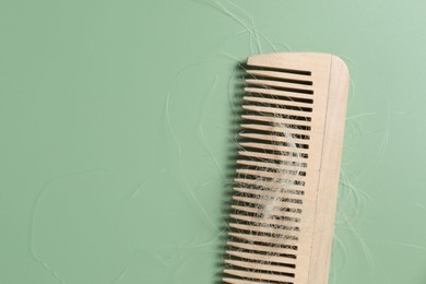 Photo of Wooden comb with lost hair on green background, top view. Space for text