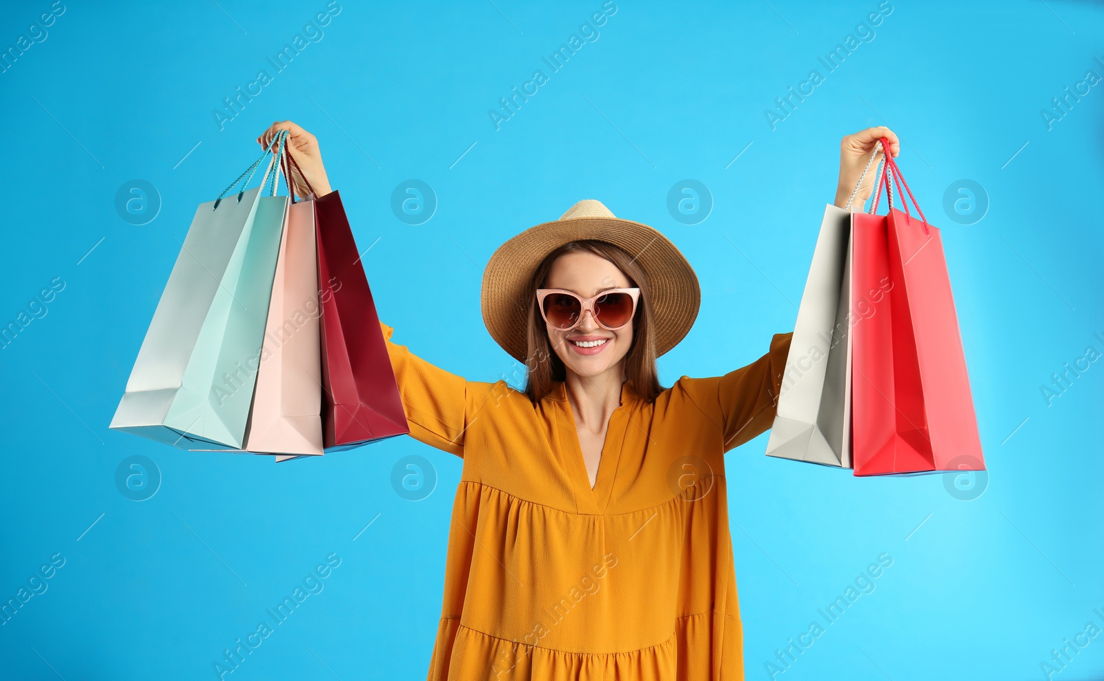 Photo of Beautiful young woman with paper shopping bags on light blue background