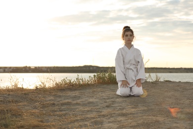 Photo of Cute little girl in kimono meditating outdoors at sunset. Karate practicing