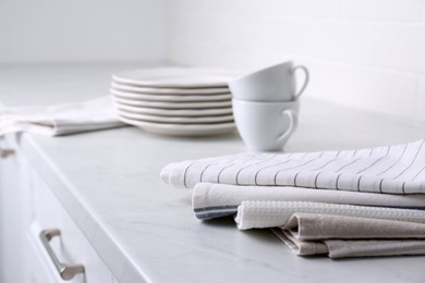 Stack of soft kitchen towels and dishware on countertop indoors, closeup. Space for text