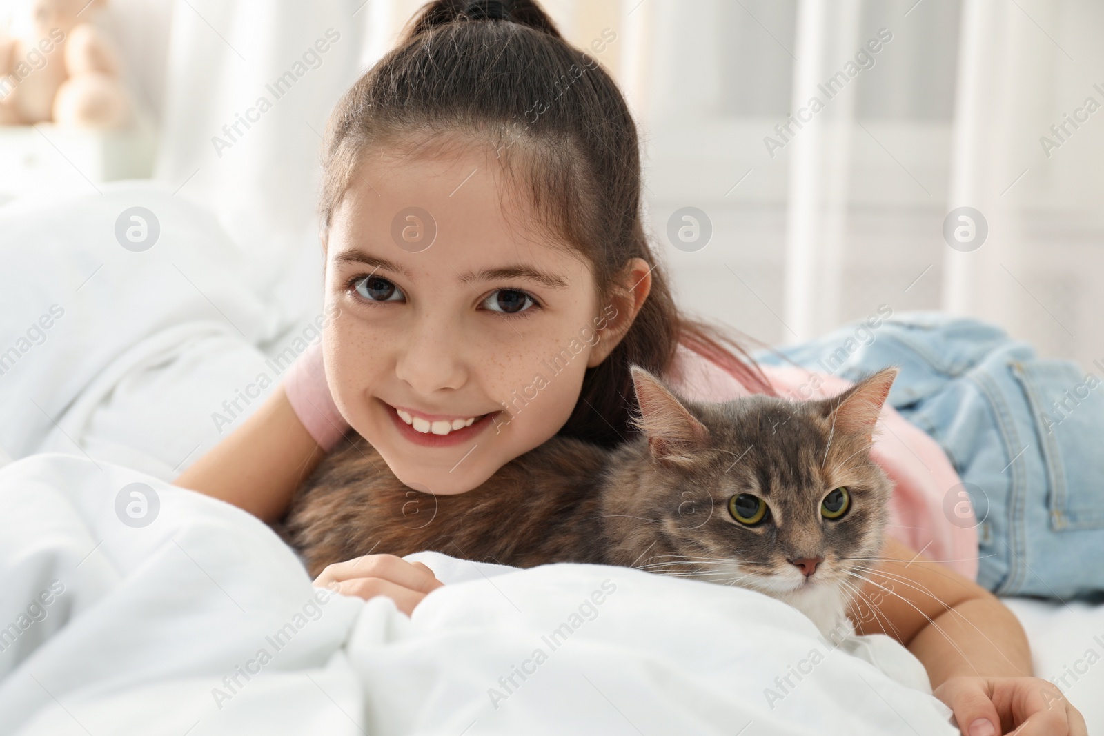 Photo of Cute little girl with cat lying on bed at home. First pet