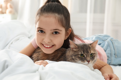 Cute little girl with cat lying on bed at home. First pet