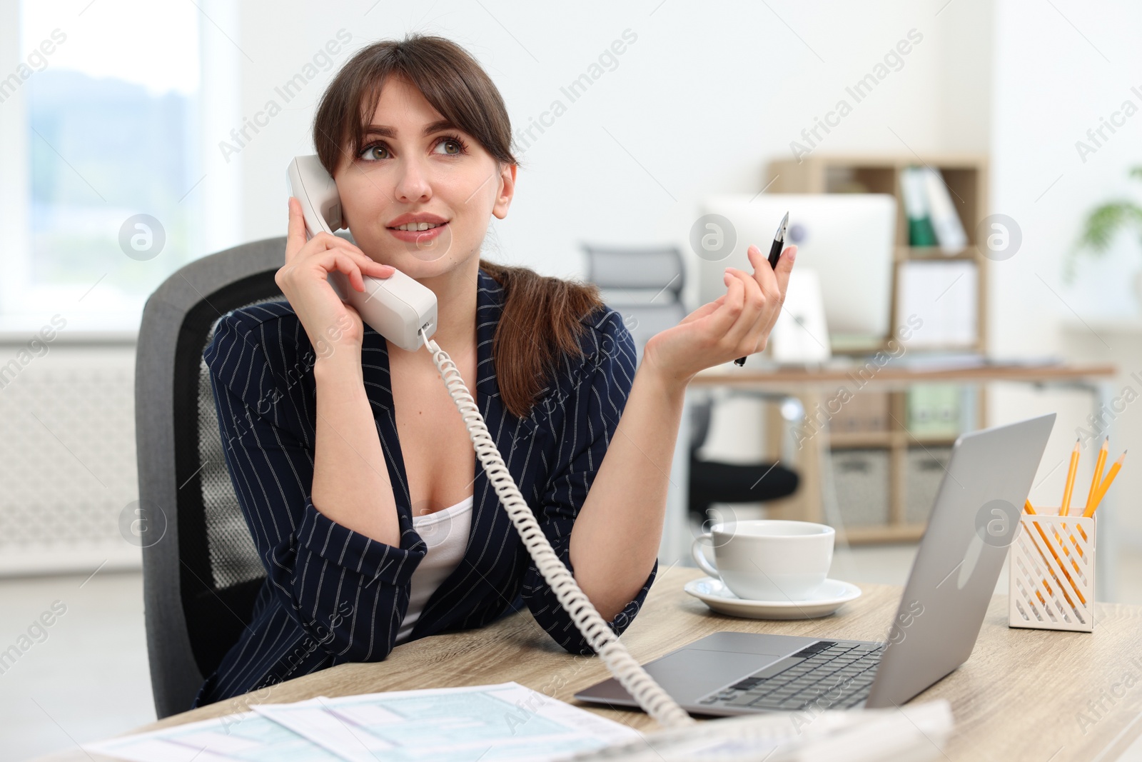 Photo of Smiling secretary talking on telephone at table in office