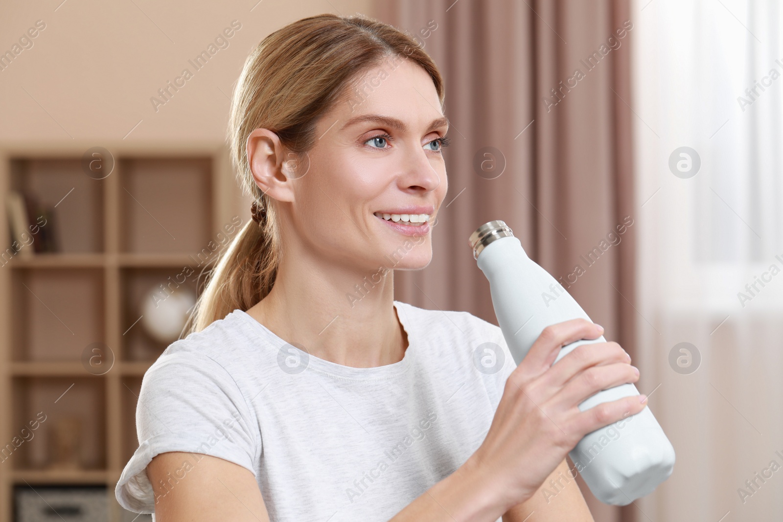 Photo of Happy woman with thermo bottle in room