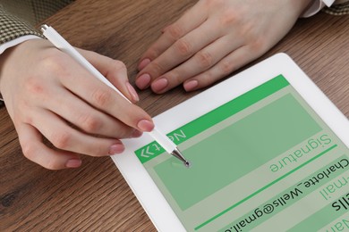 Electronic signature. Woman using stylus and tablet at wooden table, closeup