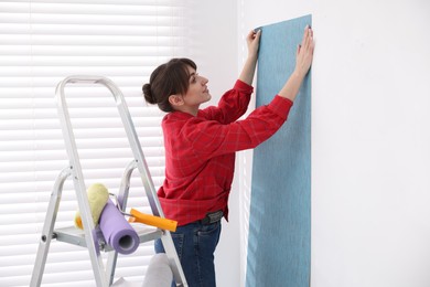 Photo of Woman hanging light blue wallpaper in room