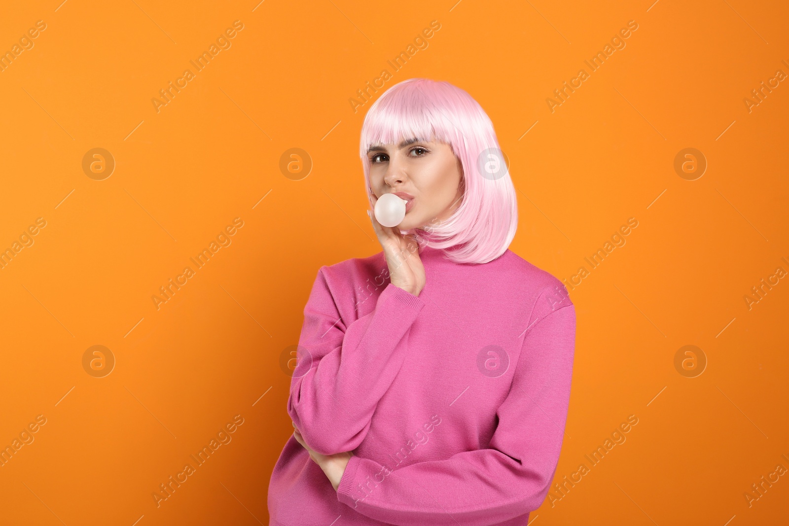 Photo of Beautiful woman blowing bubble gum on orange background