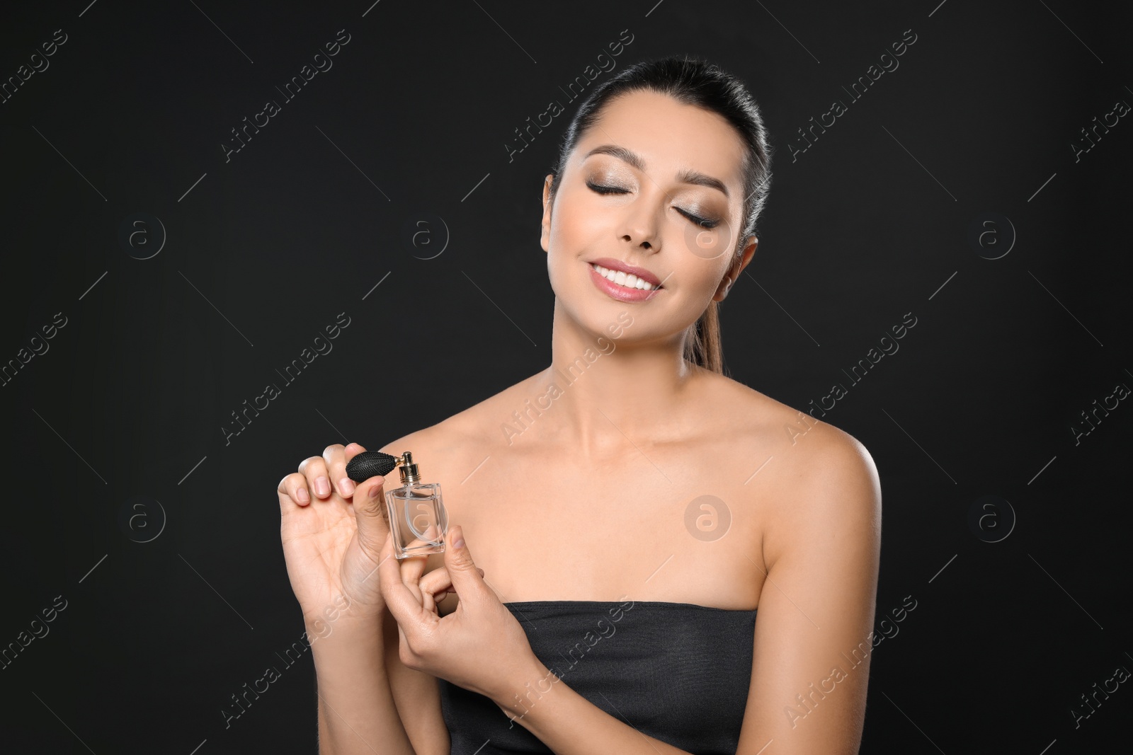 Photo of Young woman applying perfume against black background
