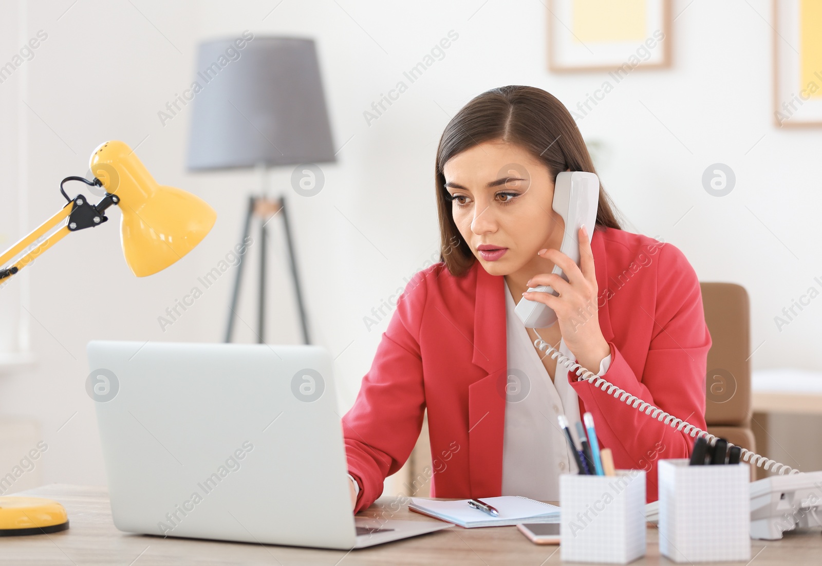 Photo of Young woman talking on phone at workplace