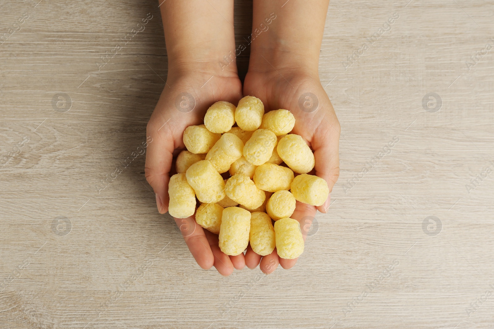 Photo of Woman holding corn sticks at wooden table, top view