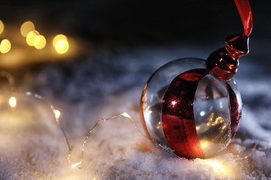 Photo of Christmas ball and fairy lights on white snow outdoors. Space for text