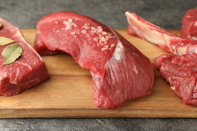 Photo of Pieces of raw beef meat and spices on grey textured table, closeup