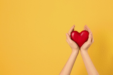 Woman holding decorative heart in hands on color background, space for text