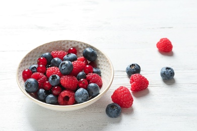 Photo of Bowl with raspberries, red currant and blueberries on wooden table