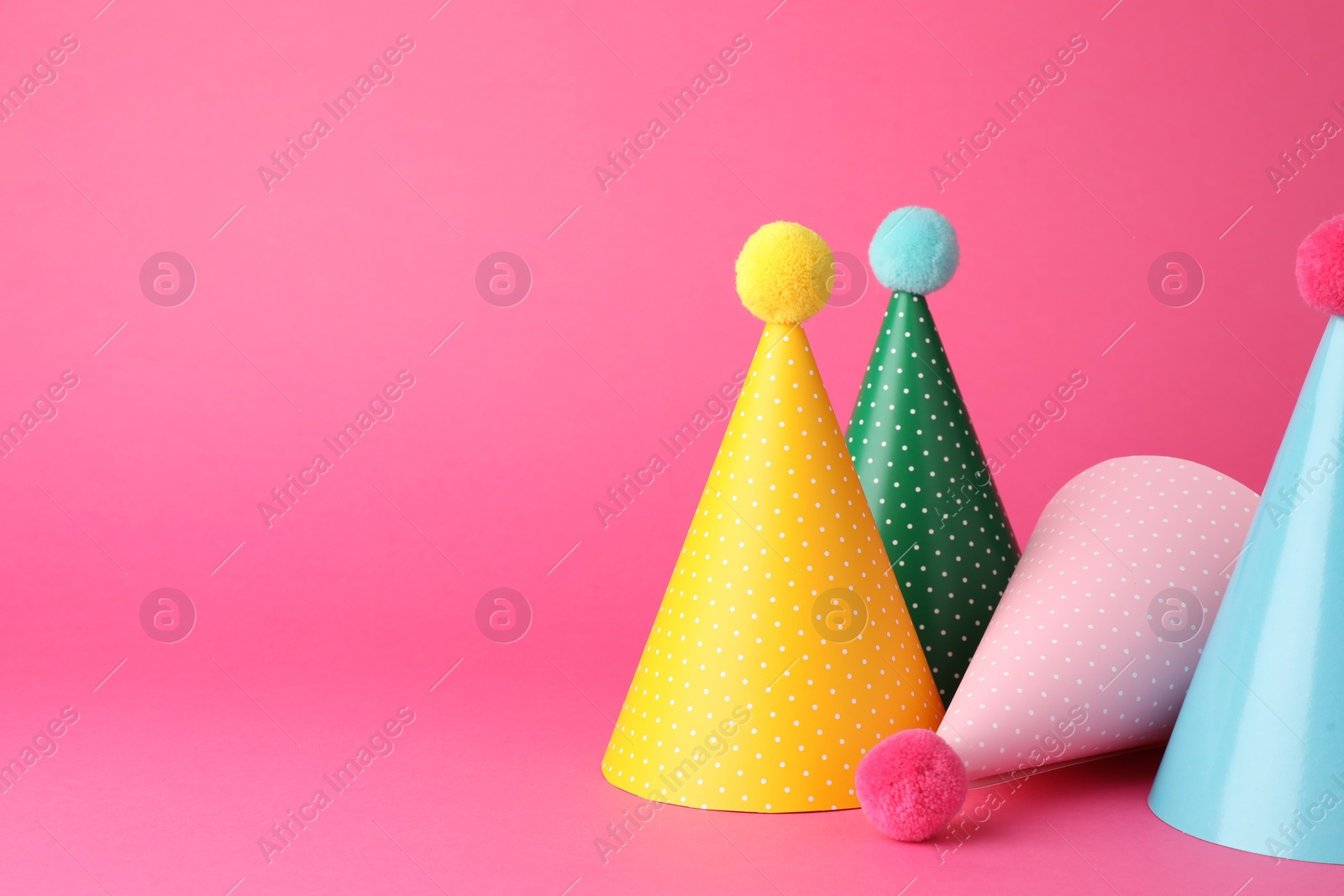 Photo of Beautiful party hats with pompoms on pink background, space for text