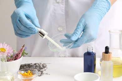 Scientist developing cosmetic oil at white table, closeup